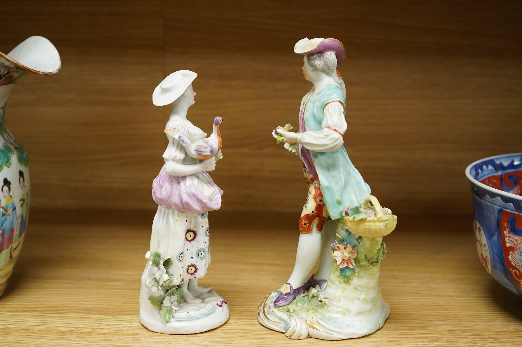 A Derby porcelain figure of a lady holding a bird, c.1760-65 and a Derby porcelain figure of a gentleman fruit seller, largest 24cm high (2)